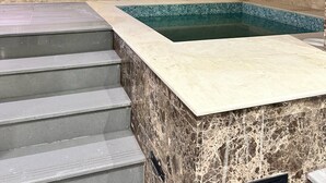 Ein Wellnessbereich mit Marmorwand, einem kleinen Pool und einer Treppe zu einer erhöhten Ebene.