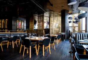 A modern restaurant interior with wooden tables and black chairs, large windows, and a high ceiling with exposed beams. - Hotel Best Day (Algiers)