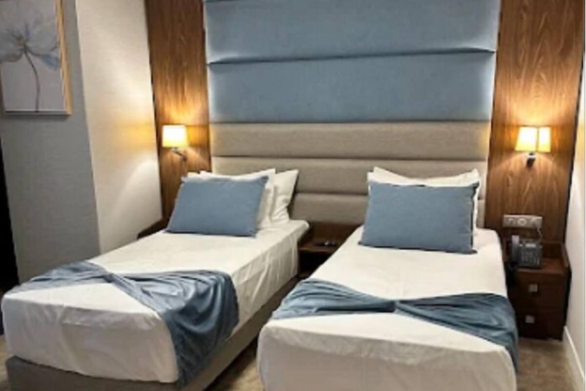 A hotel room with two beds, a wooden headboard, and two bedside lamps.