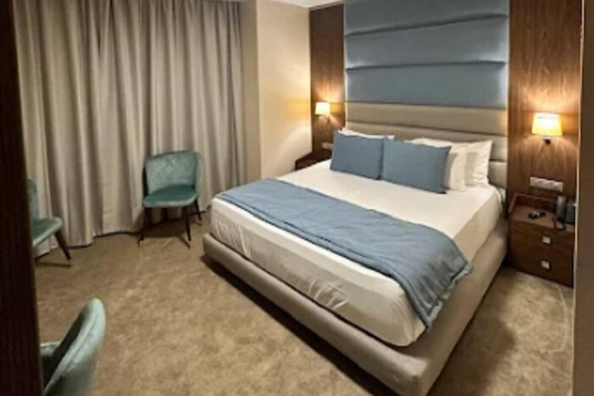 A hotel room with a large bed, a chair, a nightstand, and a ceiling light.