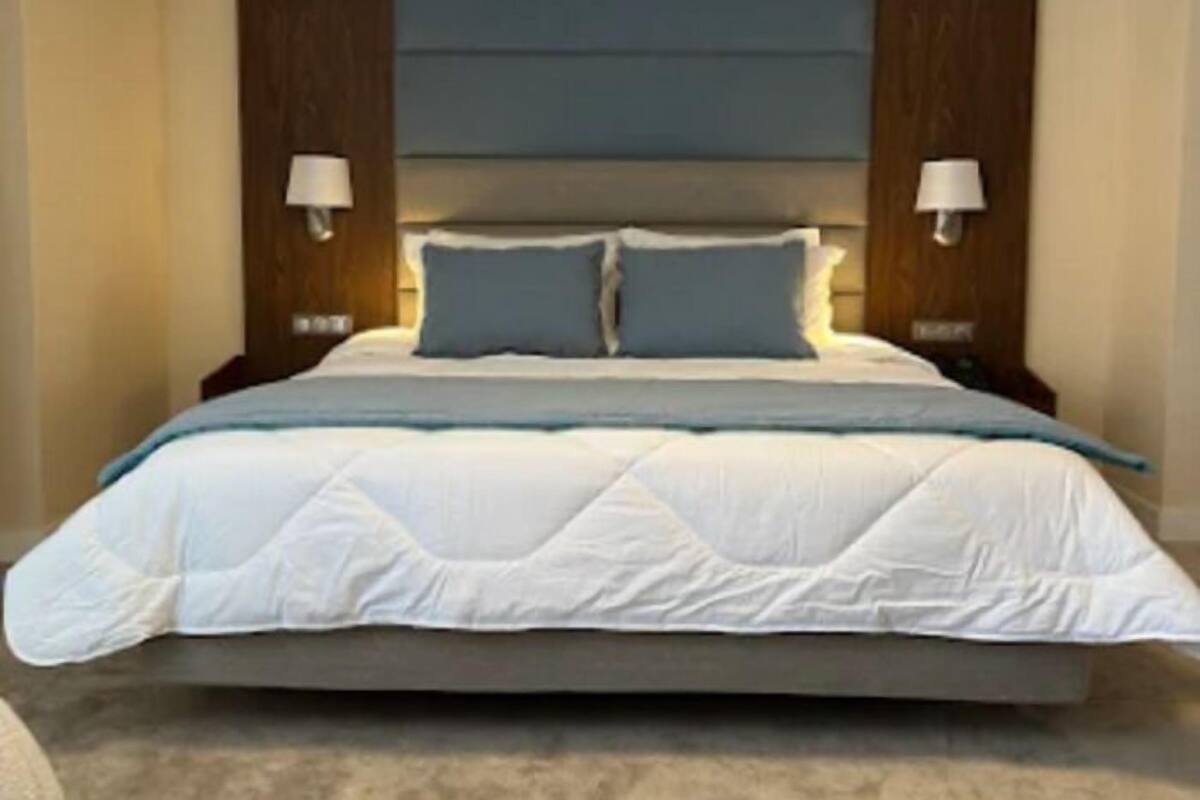 A bedroom with a large bed, two bedside lamps, and a headboard with a blue panel.