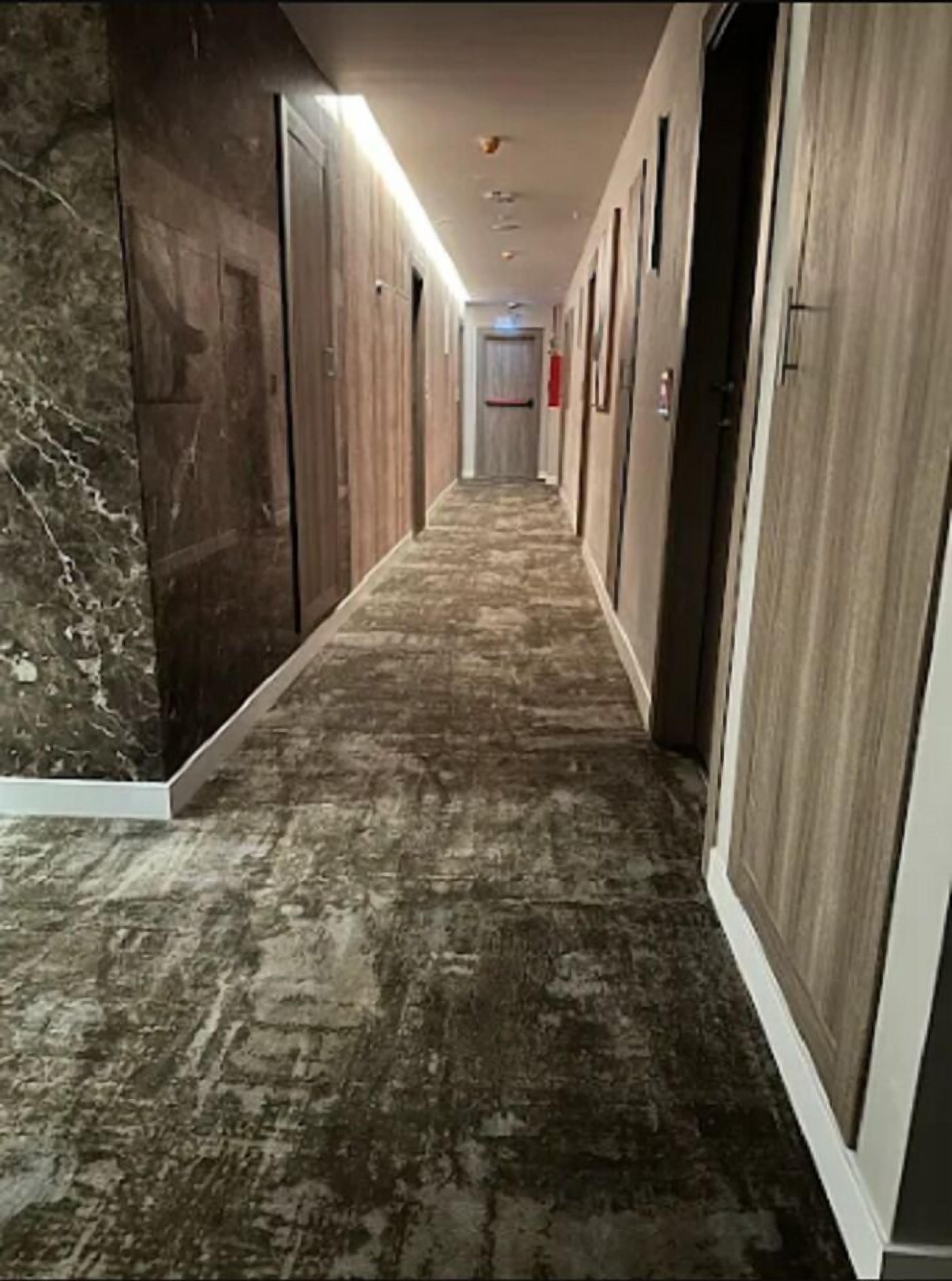 A hallway with a marble floor, wooden walls, and doors leading to rooms.