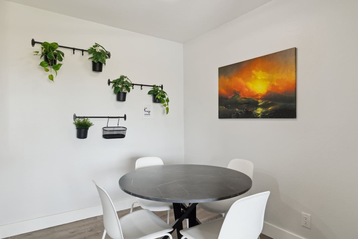 A dining area with a round table and white chairs, surrounded by potted plants on a wall-mounted rack.