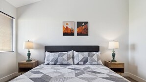 A bedroom with a bed, two nightstands, two wall-mounted lamps, and two framed artworks.