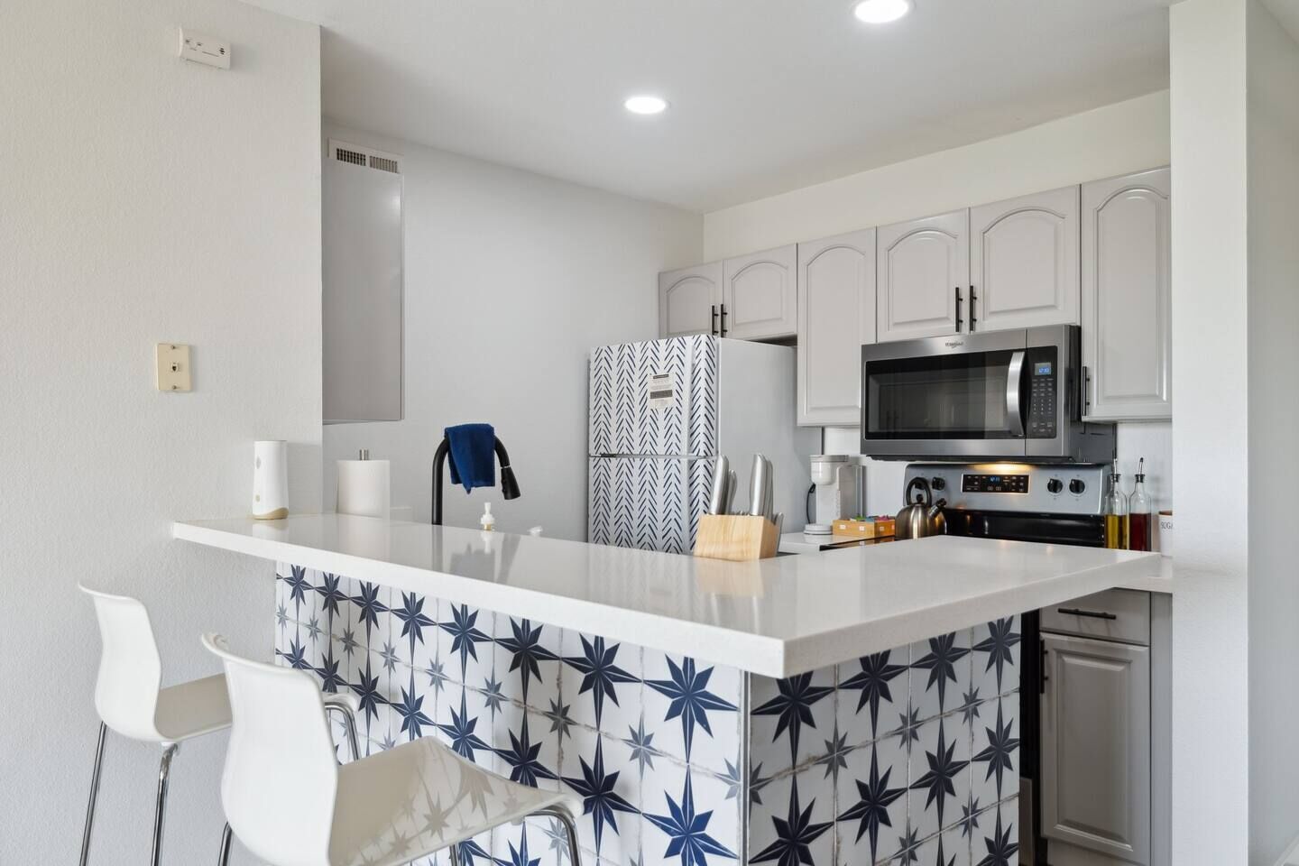 A modern kitchen with white cabinetry, a central island with a patterned backsplash, and a microwave above the stove.