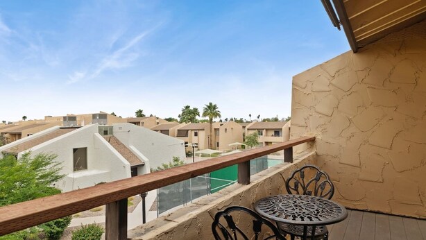 A balcony with a view of other buildings, a pool, and a table with chairs.