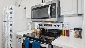 A modern kitchen with a stainless steel microwave, oven, and kettle. There are cabinets, a coffee maker, and various condiments on the counter.