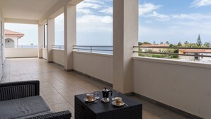 A balcony with a table set for breakfast, a view of the sea, and a building with a red roof in the background. - ApartHotel Capo Rizzuto - Sea View Apartments 40mt from the Reserved Beach (Capo Rizzuto)