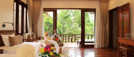 Habitación de hotel con cama, escritorio y vistas a la vegetación a través de amplias ventanas.