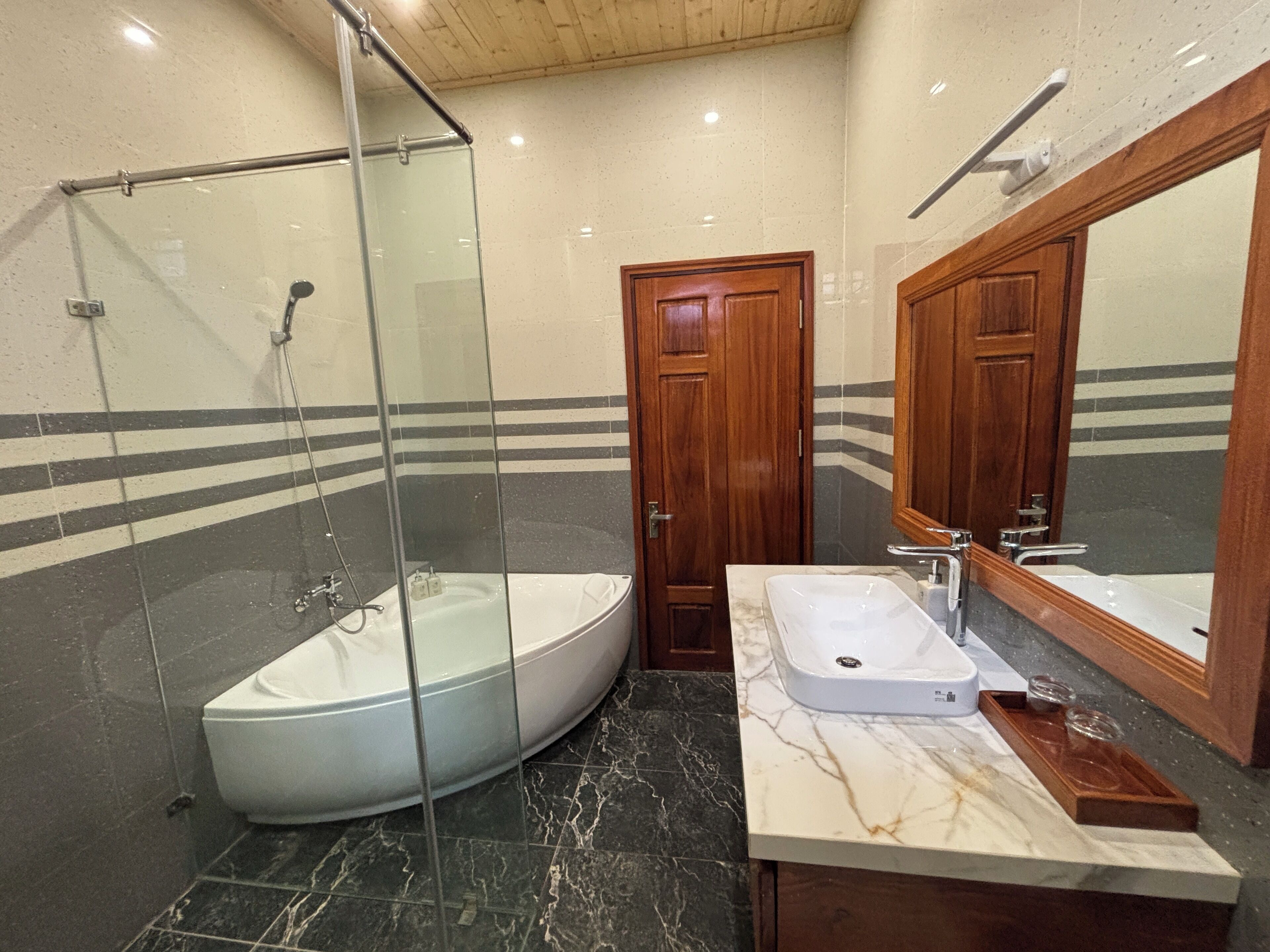 A modern bathroom with a glass-enclosed shower, a freestanding bathtub, a marble vanity, and a large mirror.