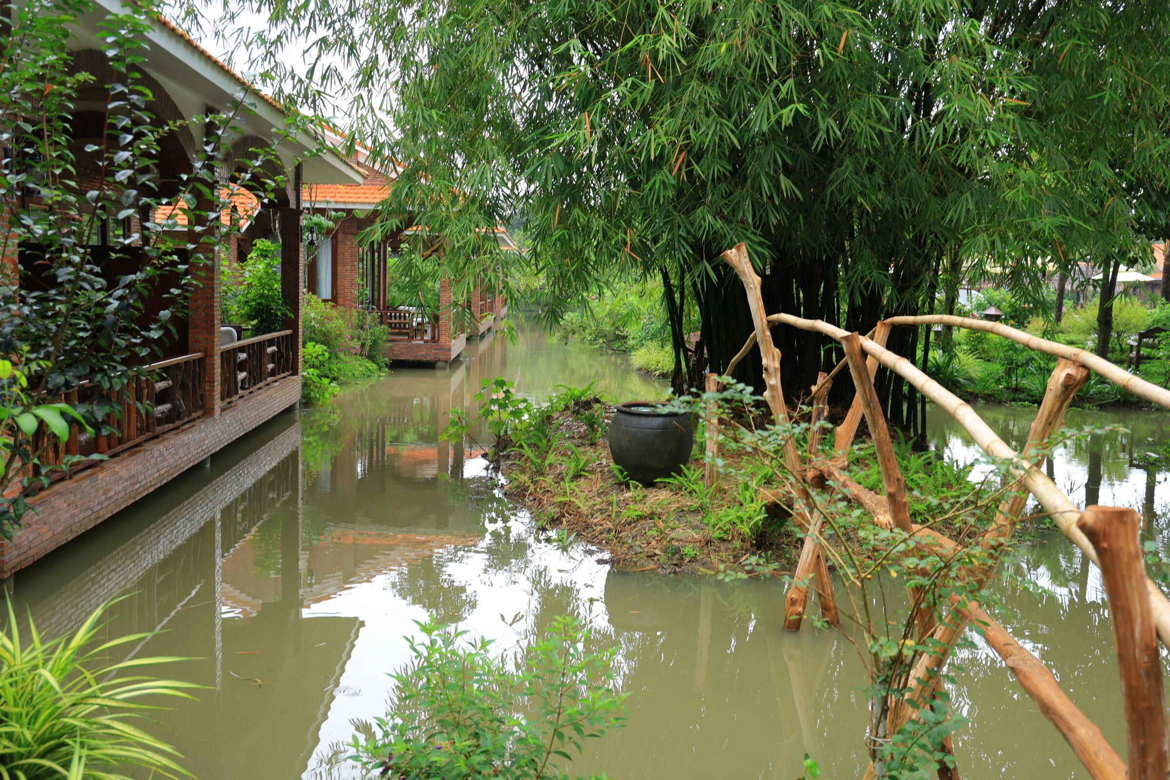 A traditional wooden bridge over a calm river, surrounded by lush greenery and bamboo.