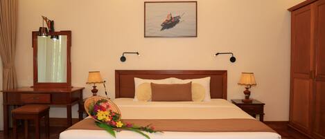 A hotel room with a large bed, a desk, a chair, a mirror, a picture on the wall, and two bedside lamps.