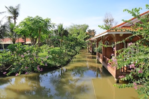 A canal with a wooden bridge, lush greenery, and a building with a tiled roof. - Phi Yen Eco Resort (Can Tho)