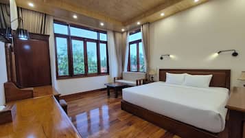 A hotel room with a wooden floor, a bed, a desk, and large windows.