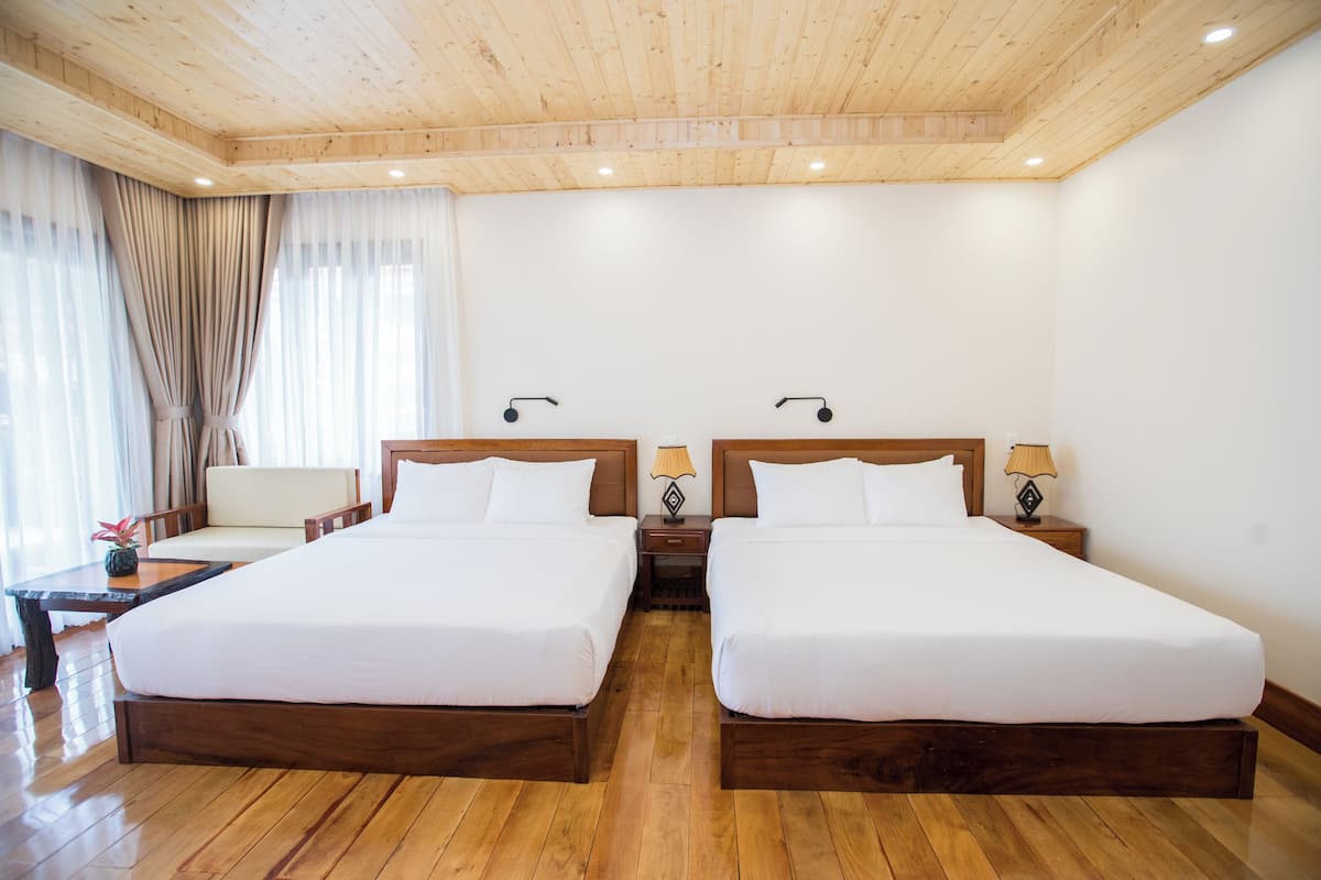 Habitación de hotel con dos camas, suelo de madera, techo de madera y una ventana con cortinas.