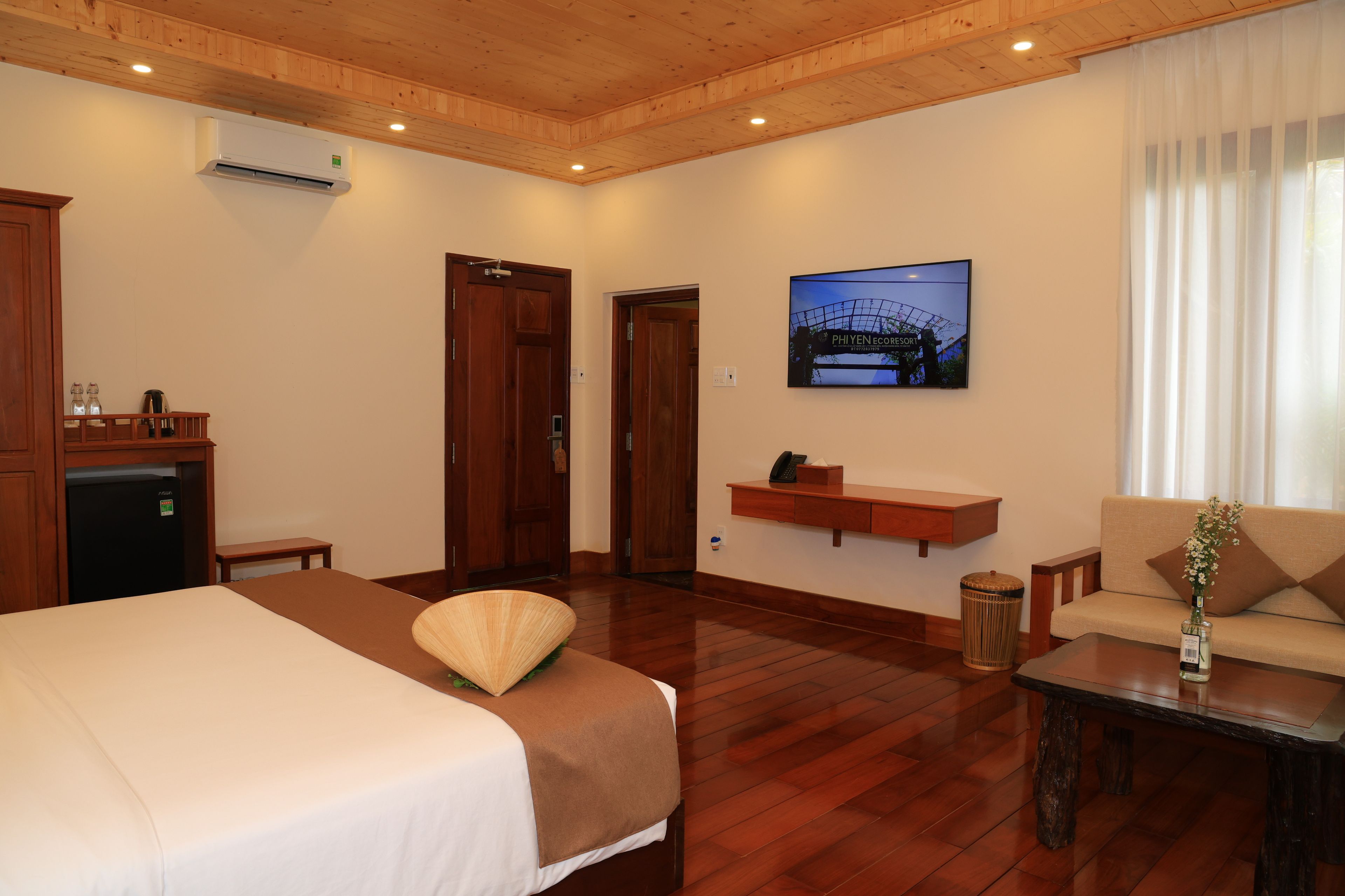 Habitación de hotel con cama, escritorio, silla, mesita, un cubo de basura, estante con teléfono y un cuadro de un puente.