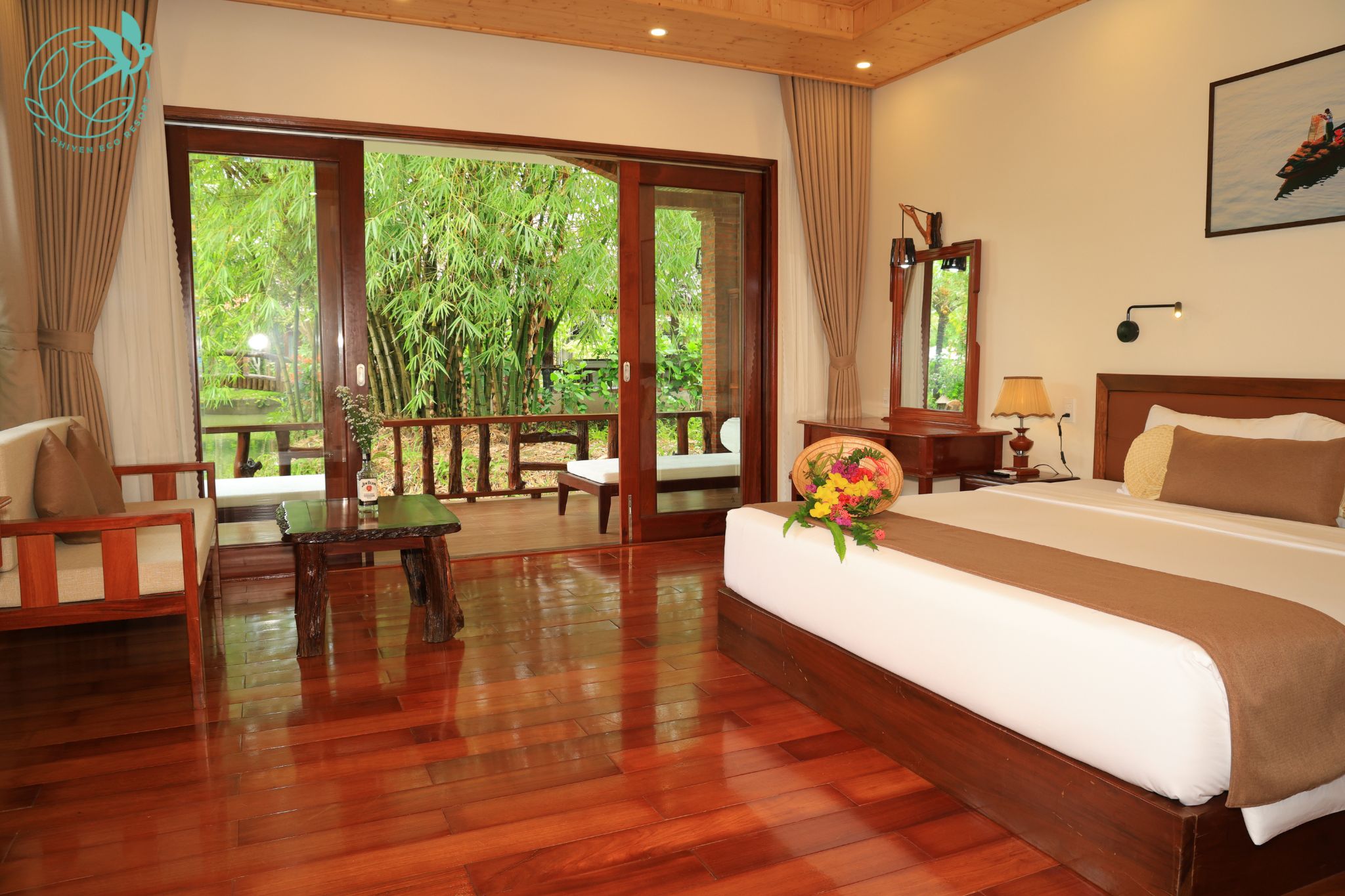 A hotel room with a large bed, a desk, a chair, and a view of greenery through a glass door.