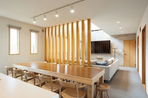 A modern dining area with a wooden table and chairs, a partition with vertical slats, and a sofa in the background.