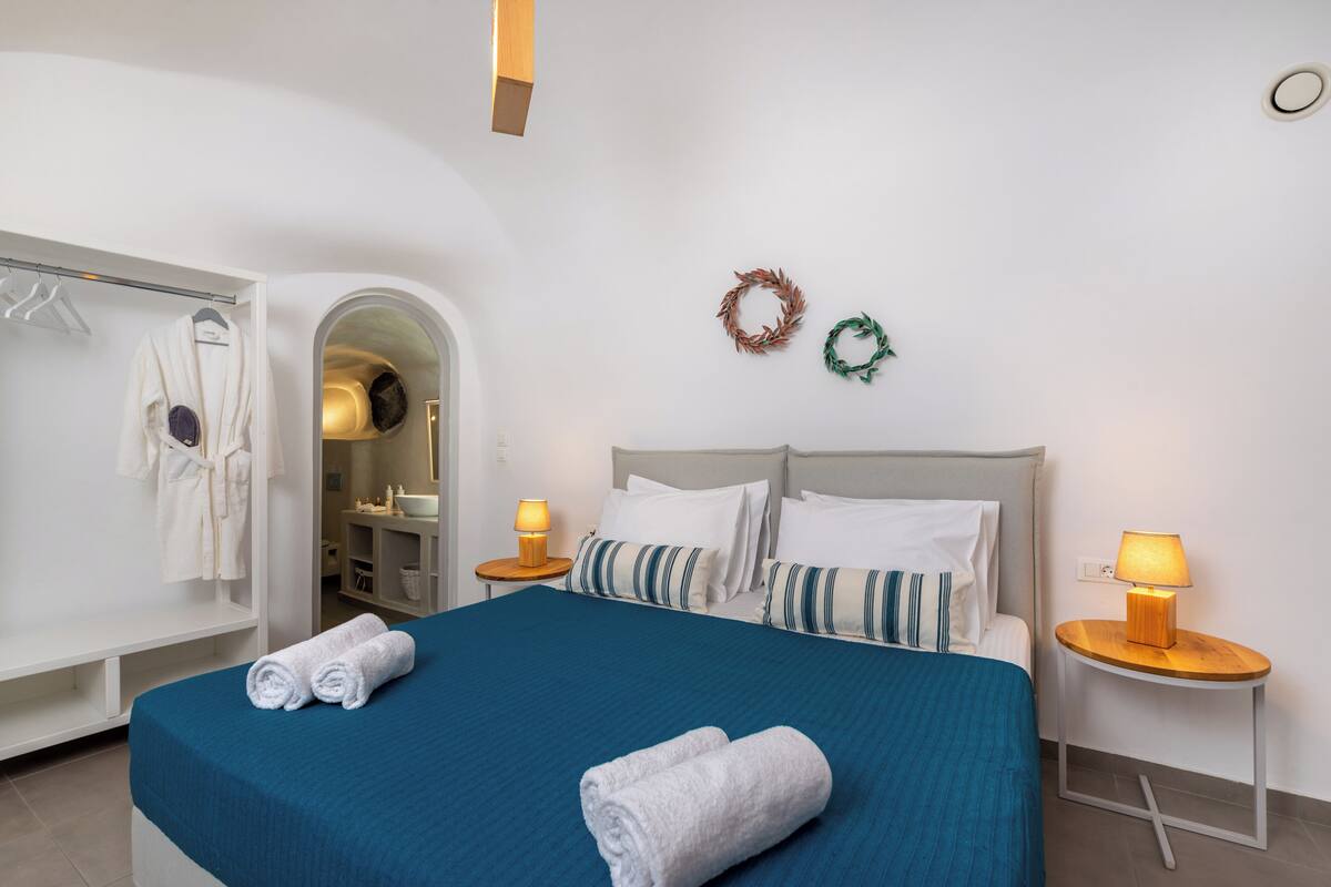 A hotel room with a bed, two bedside lamps, a robe hanging on a rack, and a mirror.