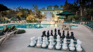 A pool area with a chessboard set up for a game, lounge chairs, and a fountain.