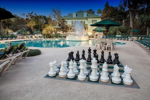 A pool area with a chessboard set up for a game, lounge chairs, and a fountain.