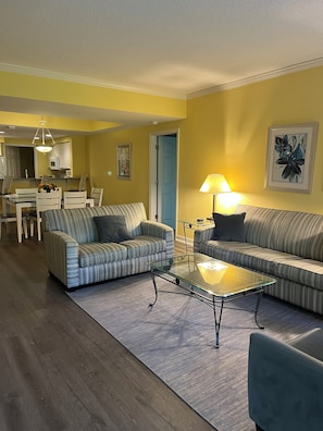 A living room with two sofas, a glass coffee table, and a dining area with chairs and a table.
