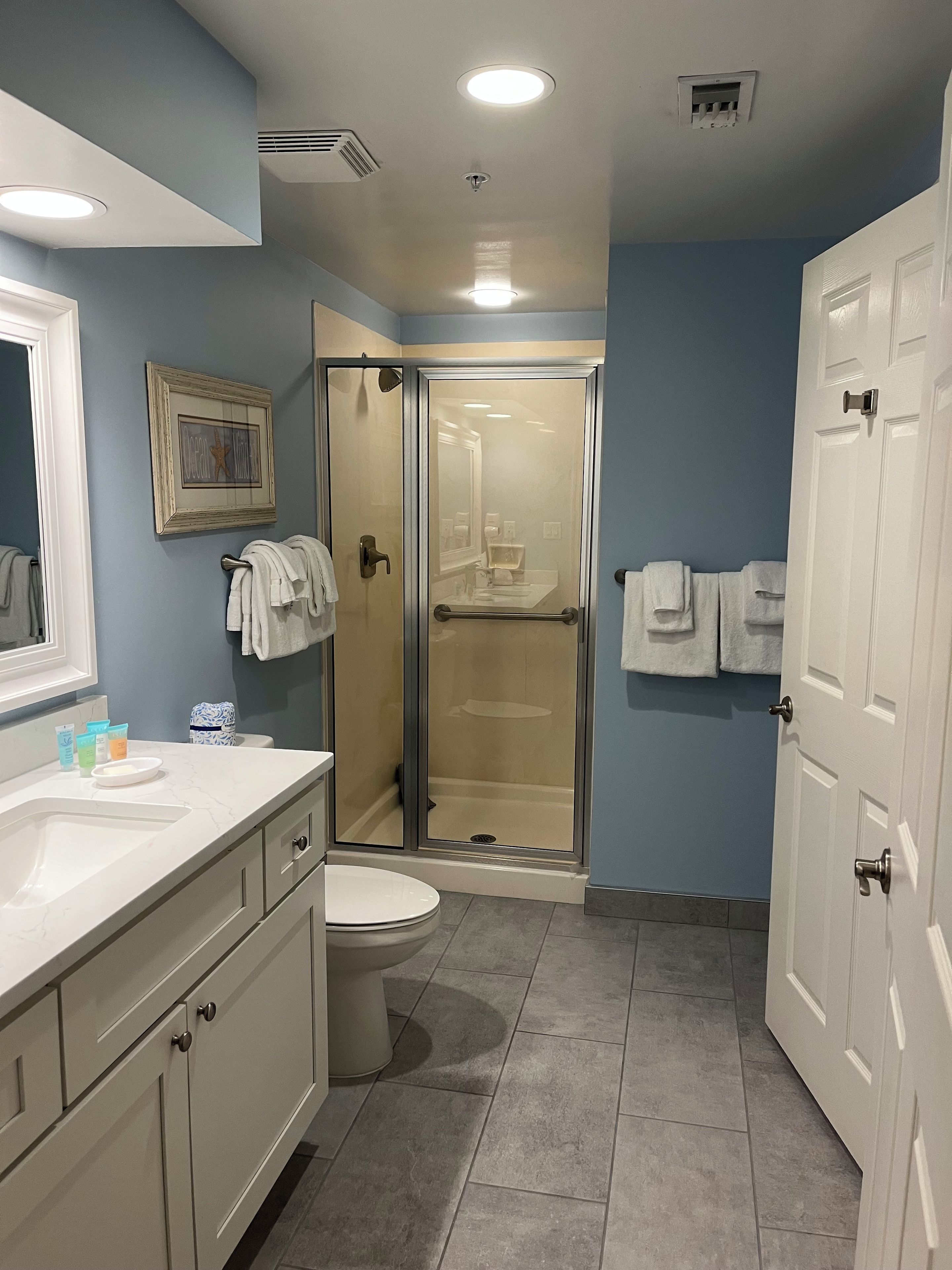 A bathroom with a toilet, sink, shower, and a glass-enclosed shower stall.