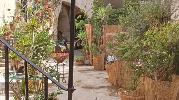 A courtyard with potted plants, outdoor seating, and a stone building with arches. - Very nice little apartment in the heart of the beautiful island of Ortigia (Siracusa)