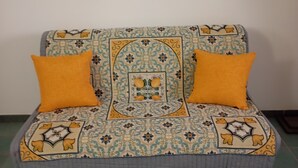 A sofa with a patterned cover and two orange cushions, placed against a plain wall. - Very nice little apartment in the heart of the beautiful island of Ortigia (Siracusa)
