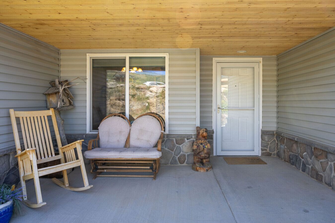 A covered porch with a wooden bench, a rocking chair, and a bear statue.