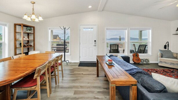 A spacious living area with a wooden dining table, a sofa, and a bench. There is a coat rack, a bookshelf, and a guitar. - Juuust Right - Gorgeous view, 5 mins from the lake (Garden City)