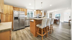 A modern kitchen with wooden cabinets, stainless steel appliances, and a bar area with patterned stools. - Juuust Right - Gorgeous view, 5 mins from the lake (Garden City)