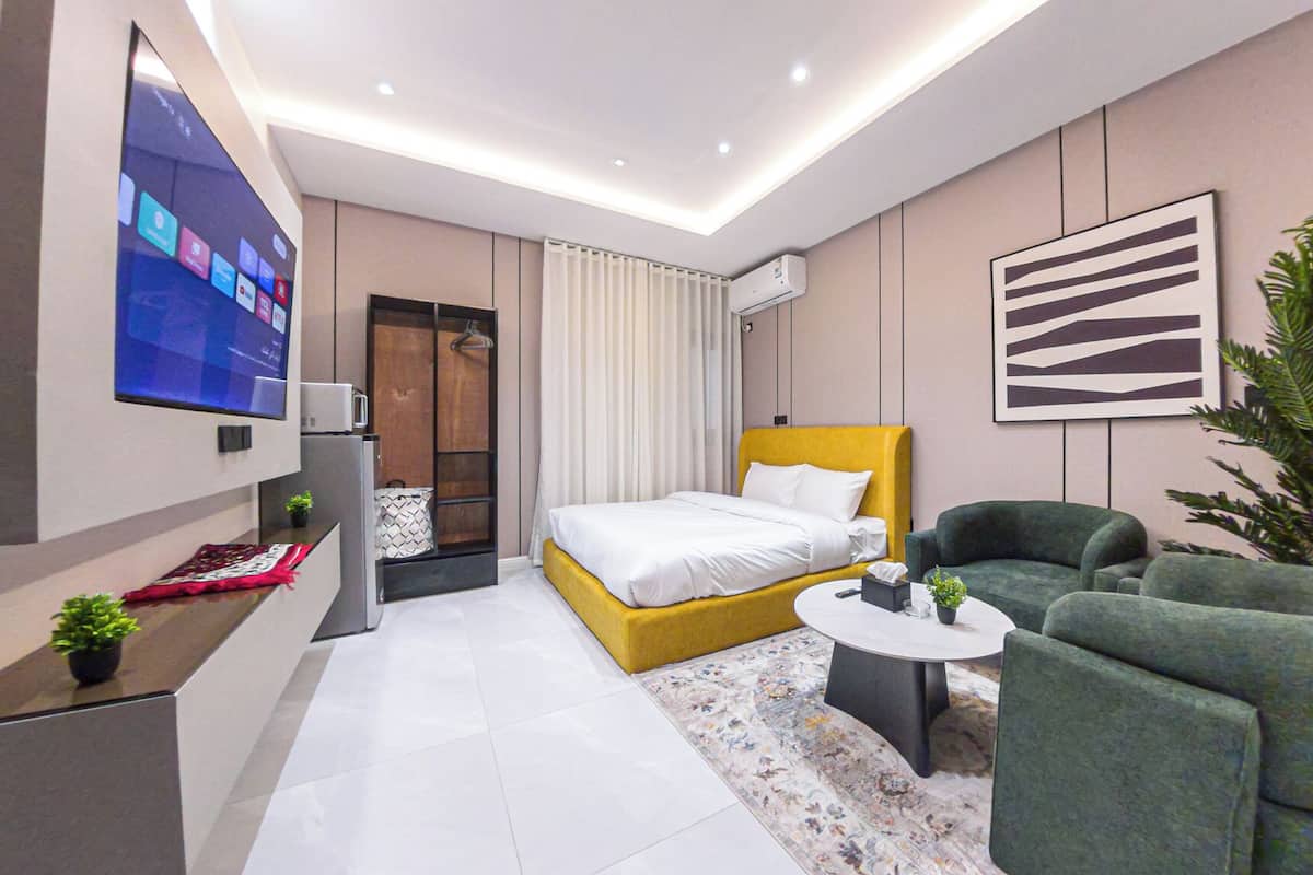 Moderni hotellihuone, jossa on sänky, sohva, televisio ja pieni pöytä.