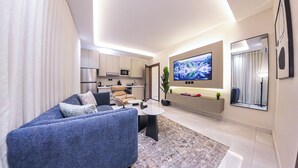 Un saló modern amb un sofà, una taula de centre i una televisió. Hi ha una zona de cuina amb armaris i electrodomèstics.