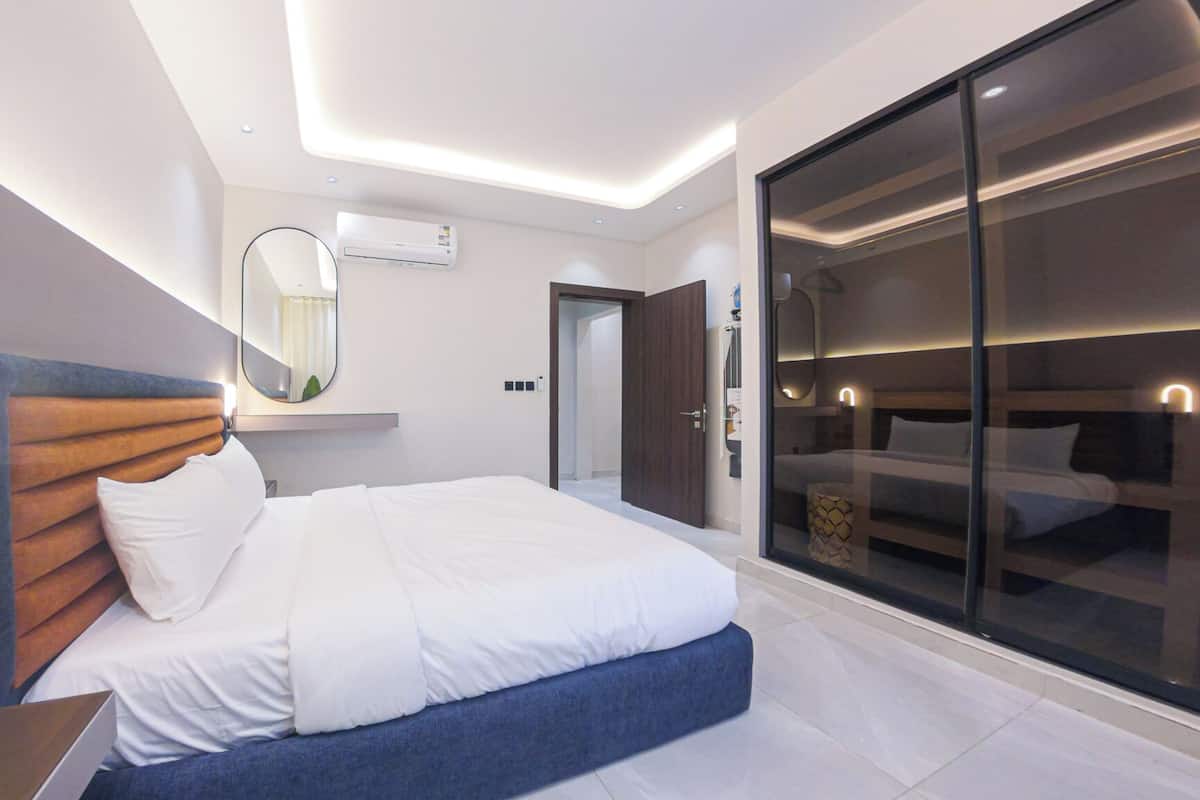 Moderni hotellihuone, jossa on suuri sänky, yöpöytä, peili ja liukuovi, joka johtaa parvekkeelle.