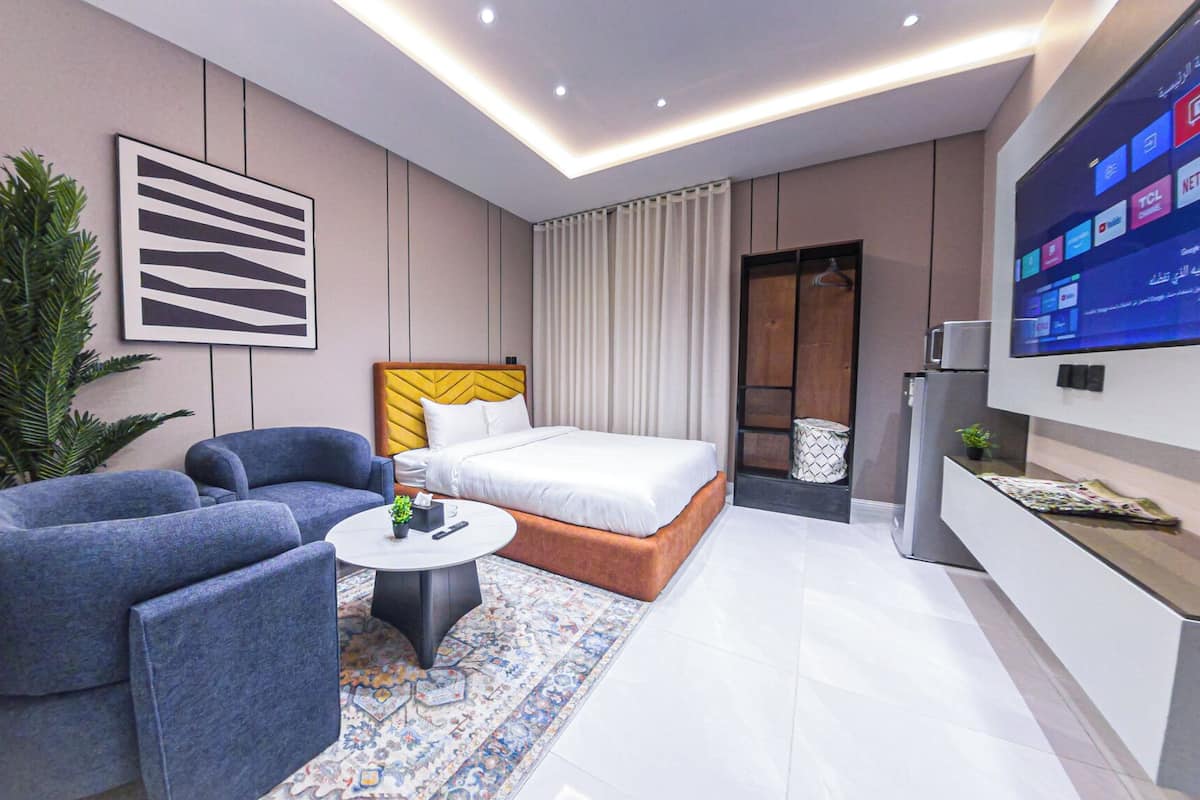 Moderni hotellihuone, jossa on sänky, kaksi sohvaa, sohvapöytä, televisio ja suuri ikkuna.