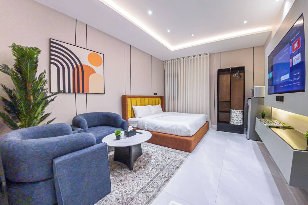 Moderni hotellihuone, jossa on sänky, sohva, sohvapöytä ja seinälle asennettu televisio.