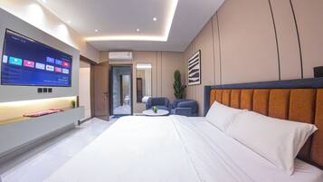 A modern hotel room with a large bed, a TV mounted on the wall, a seating area with two chairs, and a small table.