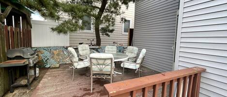 An outdoor patio with a wooden deck, a mosaic wall, and a seating area with chairs and a table.