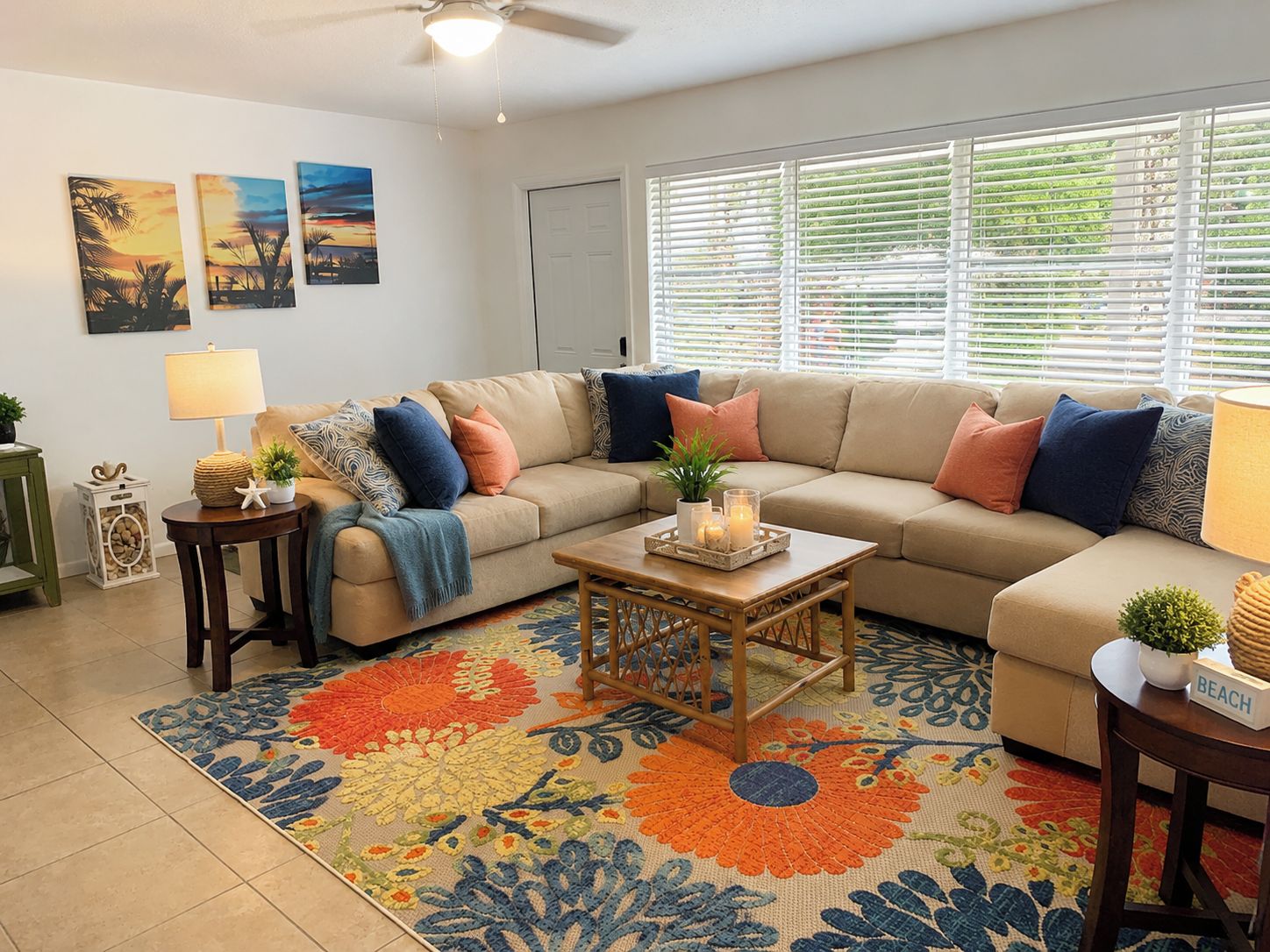 A living room with a beige sofa, a coffee table, and a colorful rug. There are wall art pieces and a window with blinds.