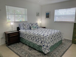 Quarto com cama, duas mesas de cabeceira, um criado-mudo, cômoda e duas janelas com persianas.