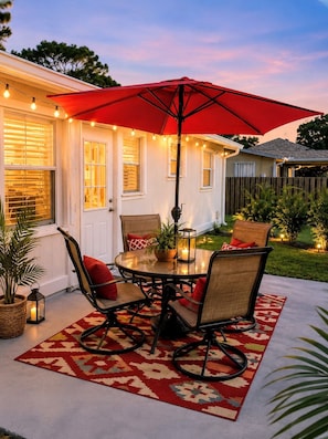An outdoor patio with a round table, chairs, and a red umbrella.