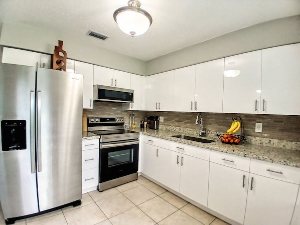A modern kitchen with stainless steel appliances, white cabinets, and a granite countertop.