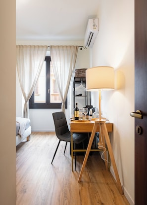 Ein Hotelzimmer mit einem Bett, einem Schreibtisch mit Lampe, einem Sessel und einem fenster mit Vorhängen.