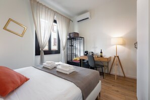 Een hotelkamer met een bed, een bureau, een stoel, een lamp en een airconditioner.