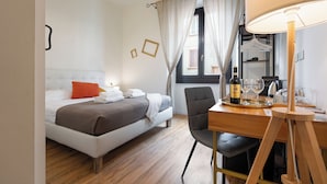 Ein Hotelzimmer mit einem Bett, einem Schreibtisch mit Stuhl, einem Spiegel, einem Fenster mit Vorhängen und einer Weinflasche.