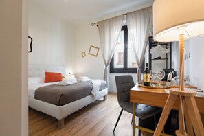 Ein Hotelzimmer mit einem Bett, einem Schreibtisch mit Stuhl, einem Spiegel, einem Fenster mit Vorhängen und einer Weinflasche.