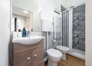 A modern bathroom with a white sink, a toilet, and a shower with a leaf-patterned shower curtain.