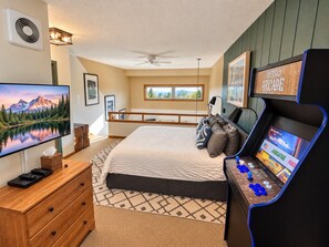 A bedroom with a bed, a television, a gaming console, and a window with a view.