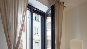 Une chambre dotée d’une porte-fenêtre coulissante donnant sur un balcon, d’une table de chevet avec une lampe et d’un miroir au mur.